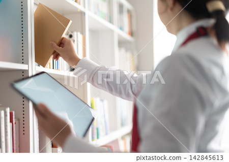 A bookstore employee using a tablet to organize bookshelves. A bookstore employee using a tablet to organize bookshelves. 142845613