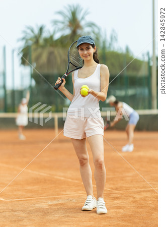 Woman in sportswear against backdrop of outdoor tennis court 142845972