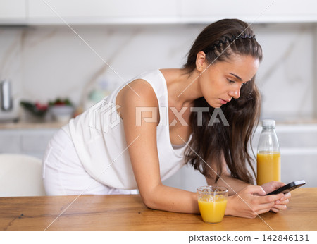 Young woman drinking juice and scrolling through social media on mobile 142846131