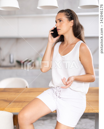 Young woman talking on mobile phone in kitchen Young woman talking on mobile phone in kitchen 142846176
