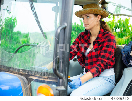 Concentrated girl farmer is sitting at the wheel of a tractor Concentrated girl farmer is sitting at the wheel of a tractor 142846210