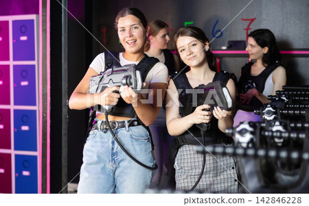 Portrait of two positive girls in special vests playing laser tag with friends on bachelorette Portrait of two positive girls in special vests playing laser tag with friends on bachelorette 142846228