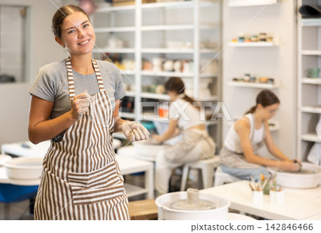 Girl takes break, stands and rests, waves hello with her hands stained with clay during pottery class Girl takes break, stands and rests, waves hello with her hands stained with clay during pottery class 142846466