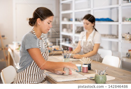 Girl kneads piece of raw clay with her hands, removes excess parts of material Girl kneads piece of raw clay with her hands, removes excess parts of material 142846486
