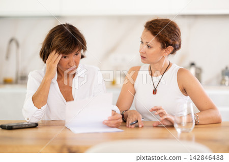 Two woman at table and trying to figure out finance problem and thinking about bills at home Two woman at table and trying to figure out finance problem and thinking about bills at home 142846488