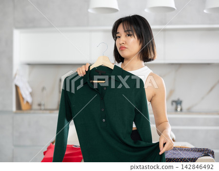 Sad young Asian girl trying to choose a dress in the kitchen Sad young Asian girl trying to choose a dress in the kitchen 142846492