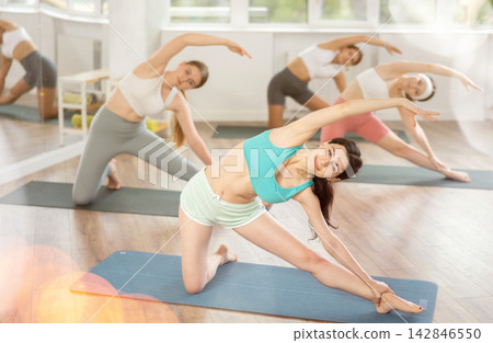 Young female teacher working out Parighasana with students group Young female teacher working out Parighasana with students group 142846550