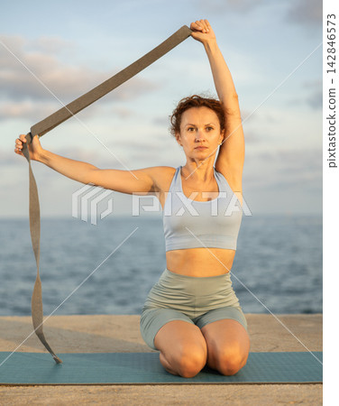Atletic woman doing yoga with stretch band on seashore Atletic woman doing yoga with stretch band on seashore 142846573