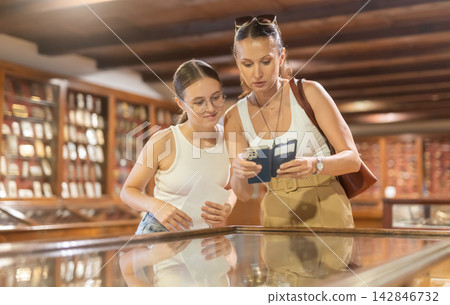 Woman with smartphone and teenage girl looking at exhibit in museum display Woman with smartphone and teenage girl looking at exhibit in museum display 142846732