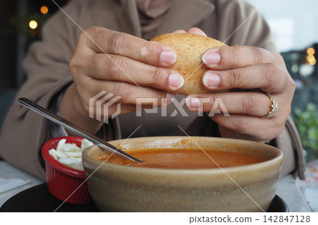 Hands holding bread above a bowl of soup with a side of salad Hands holding bread above a bowl of soup with a side of salad 142847128