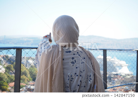 Woman points towards a distant view from a balcony with a cityscape below Woman points towards a distant view from a balcony with a cityscape below 142847150