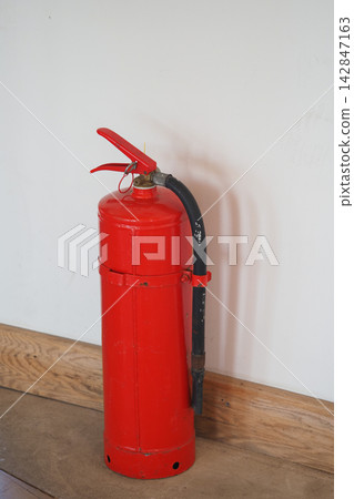 Fire extinguisher placed against a wall in a room with wooden flooring Fire extinguisher placed against a wall in a room with wooden flooring 142847163