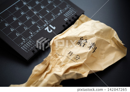 黑色背景上放著一個皺巴巴的工資信封和一張六月的日曆。 黑色背景上放著一個皺巴巴的工資信封和一張六月的日曆。 142847265