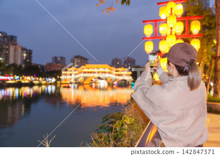 Happy woman traveler travel in Chengdu city. Tourist sightseeing and taking photo to Anshun Bridge by mobile phone at night. Famous Landmark for tourism attraction in Sichuan, China Happy woman traveler travel in Chengdu city. Tourist sightseeing and taking photo to Anshun Bridge by mobile phone at night. Famous Landmark for tourism attraction in Sichuan, China 142847371