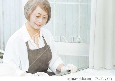 A senior woman wiping down surfaces in the living room. A senior woman wiping down surfaces in the living room. 142847584