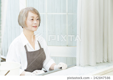 A senior woman wiping down surfaces in the living room. A senior woman wiping down surfaces in the living room. 142847586