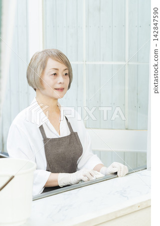 一位老婦人正在擦拭客廳裡的各種表面。 142847590