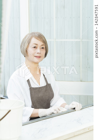 A senior woman wiping down surfaces in the living room. 142847591