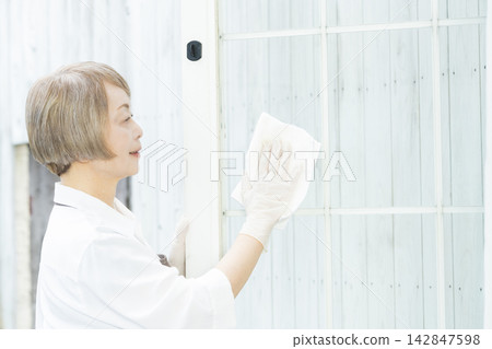 A senior woman wiping down surfaces in the living room. A senior woman wiping down surfaces in the living room. 142847598
