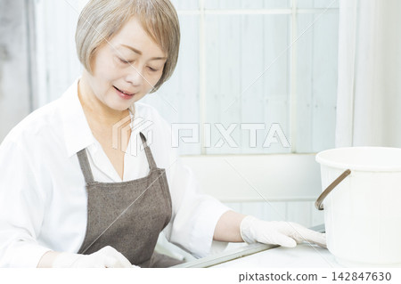 A senior woman wiping down surfaces in the living room. A senior woman wiping down surfaces in the living room. 142847630