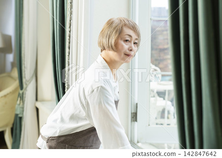 A senior woman wiping down surfaces in the living room. A senior woman wiping down surfaces in the living room. 142847642
