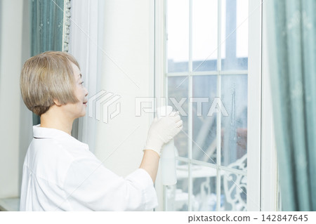 一位老婦人正在擦拭客廳裡的各種表面。 142847645
