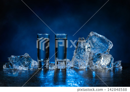 Shot glasses of vodka with ice shards on a dark blue background. Shot glasses of vodka with ice shards on a dark blue background. 142848588