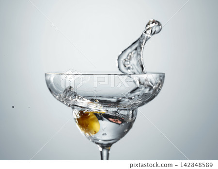 Clear martini glass with green olive in motion. Clear martini glass with green olive in motion. 142848589