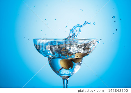 A green olives drops into a martini glass, creating a beautiful splash. A green olives drops into a martini glass, creating a beautiful splash. 142848590