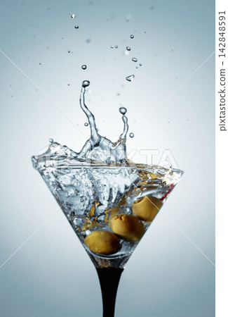 A green olives drops into a martini glass, creating a beautiful splash. A green olives drops into a martini glass, creating a beautiful splash. 142848591