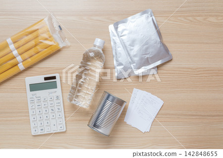 一張災難準備支出和家庭預算管理的圖片,圖中擺放著緊急食品和水儲備、計算器和收據。 一張災難準備支出和家庭預算管理的圖片,圖中擺放著緊急食品和水儲備、計算器和收據。 142848655
