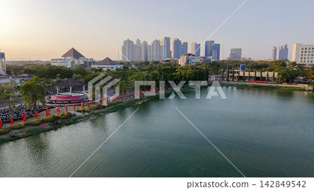 Scenic panoramic view of Danau UNESA lake surrounded by green trees and city skyline in Surabaya, East Java, Indonesia. Scenic panoramic view of Danau UNESA lake surrounded by green trees and city skyline in Surabaya, East Java, Indonesia. 142849542