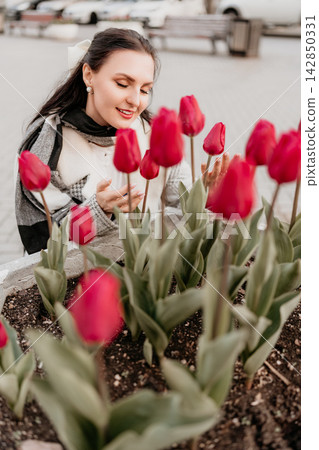 Woman tulips spring lifestyle portrait of a young brunette woman admiring red flowers in a city park planter 142850331