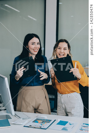 Two businesswomen discussing work using a laptop in a modern office lounge area, showing teamwork and communication Two businesswomen discussing work using a laptop in a modern office lounge area, showing teamwork and communication 142850474