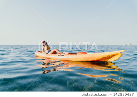Kayaking Woman Sea - A woman sits in a yellow kayak on a calm blue sea. She is enjoying a relaxing day of kayaking. Kayaking Woman Sea - A woman sits in a yellow kayak on a calm blue sea. She is enjoying a relaxing day of kayaking. 142850487