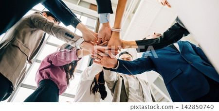 A down perspective reveals four diverse businesspeople standing in a circle stacking their hands. This image conveys the concepts of unity teamwork and global collaboration. A down perspective reveals four diverse businesspeople standing in a circle stacking their hands. This image conveys the concepts of unity teamwork and global collaboration. 142850740
