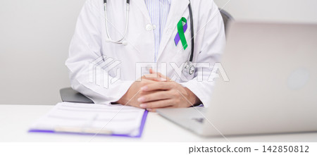 doctor using laptop and report notes on notebook. purple and green ribbon concept of March Anal Cancer Awareness month, Colorectal and Colon Cancer, Healthcare and February world cancer day doctor using laptop and report notes on notebook. purple and green ribbon concept of March Anal Cancer Awareness month, Colorectal and Colon Cancer, Healthcare and February world cancer day 142850812