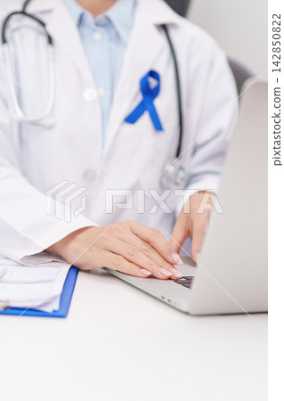 doctor using laptop and report notes on notebook. Navy blue ribbon concept of March Colorectal and Colon Cancer Awareness month, May Arthritis awareness, July Juvenile arthritis and Childhood 142850822