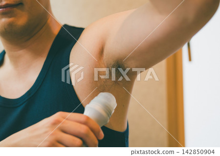 一位四十多歲的男子正在仔細地往腋下塗抹除臭劑。 一位四十多歲的男子正在仔細地往腋下塗抹除臭劑。 142850904