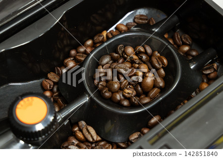 Roasted coffee beans filling the hopper and measuring scoop of an automatic espresso machine Roasted coffee beans filling the hopper and measuring scoop of an automatic espresso machine 142851840