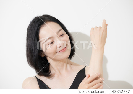 A woman in her 50s cares for her arms with her hands; a middle-aged woman performs anti-aging care, sunscreen, skincare, and lymphatic massage. A woman in her 50s cares for her arms with her hands; a middle-aged woman performs anti-aging care, sunscreen, skincare, and lymphatic massage. 142852787
