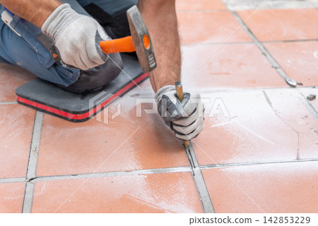 Manual demolition of ceramic flooring using a hammer and metal chisel before replacing the old floor covering. Manual demolition of ceramic flooring using a hammer and metal chisel before replacing the old floor covering. 142853229