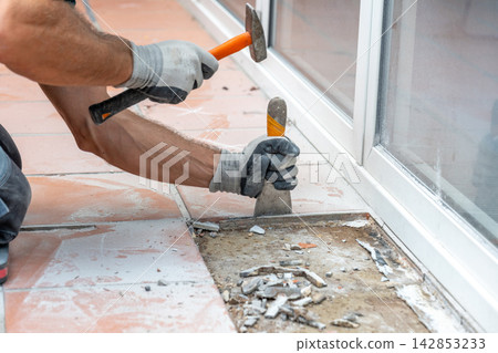 Builder manually dismantles tiled flooring and exposes the underlying base during renovation and repair work. Builder manually dismantles tiled flooring and exposes the underlying base during renovation and repair work. 142853233