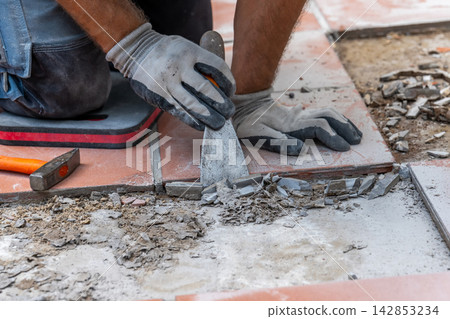 Worker wearing protective gloves cleans the floor base with a scraper after removing old ceramic tiles. Worker wearing protective gloves cleans the floor base with a scraper after removing old ceramic tiles. 142853234
