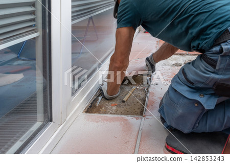 Construction worker removes damaged tiles and exposes the base before restoring the floor surface. Construction worker removes damaged tiles and exposes the base before restoring the floor surface. 142853243