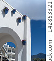 White Mediterranean arch decorated with blue flower pots against a deep blue sky in a traditional Andalusian coastal village with mountain backdrop. Balcon de Europa location. 142853321