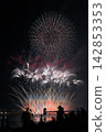 Fireworks soaring into the night sky; fireworks blooming in the summer night sky; fireworks blooming in the night sky; a fireworks display shining brightly; people watching the fireworks. 142853353