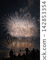 Fireworks soaring into the night sky; fireworks blooming in the summer night sky; fireworks blooming in the night sky; a fireworks display shining brightly; people watching the fireworks. 142853354