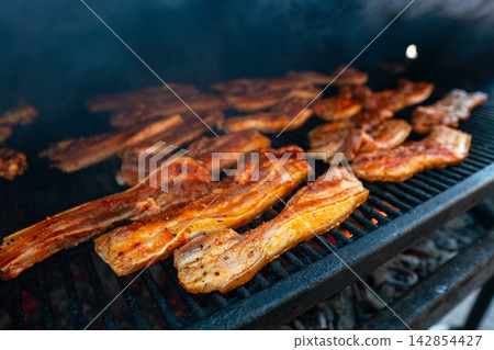 Marinated pork belly grilling over open flame with smoky flavor. Outdoor BBQ 142854427