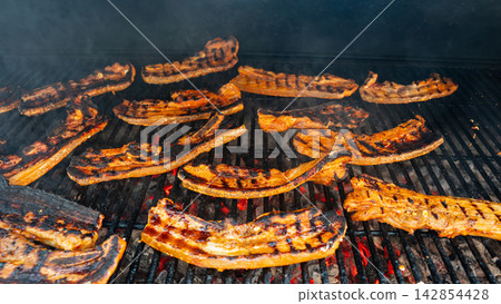 Pork belly strips grilling over open flame with smoky crispy texture 142854428